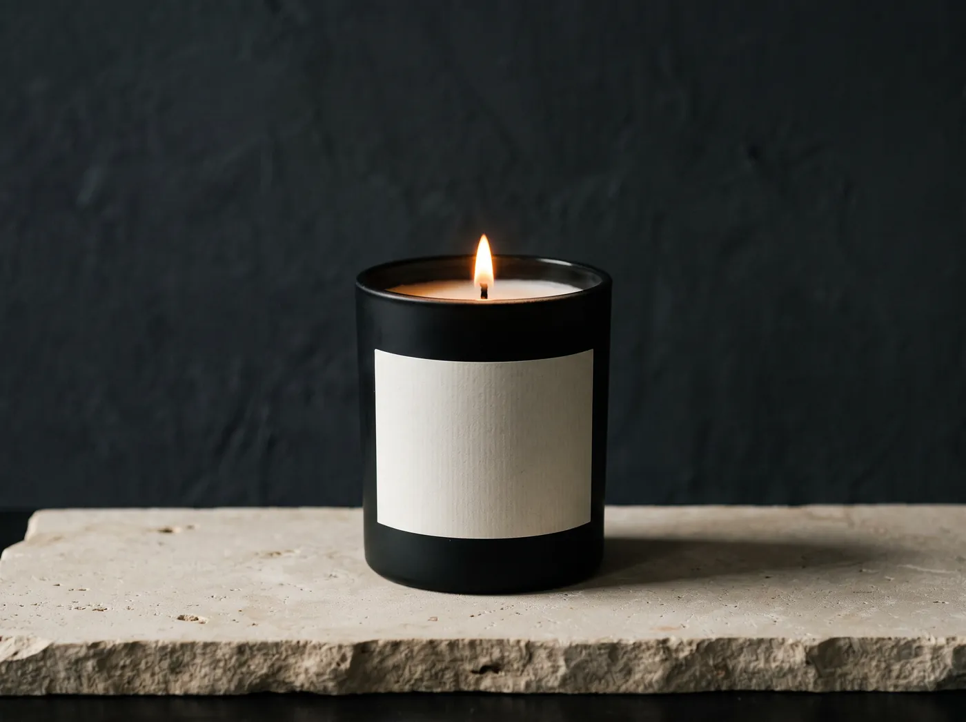 A lit candle in a matte black apothecary vessel wrapped in a plain unprinted paper label, shot low key. Vessel study, not a product photograph.